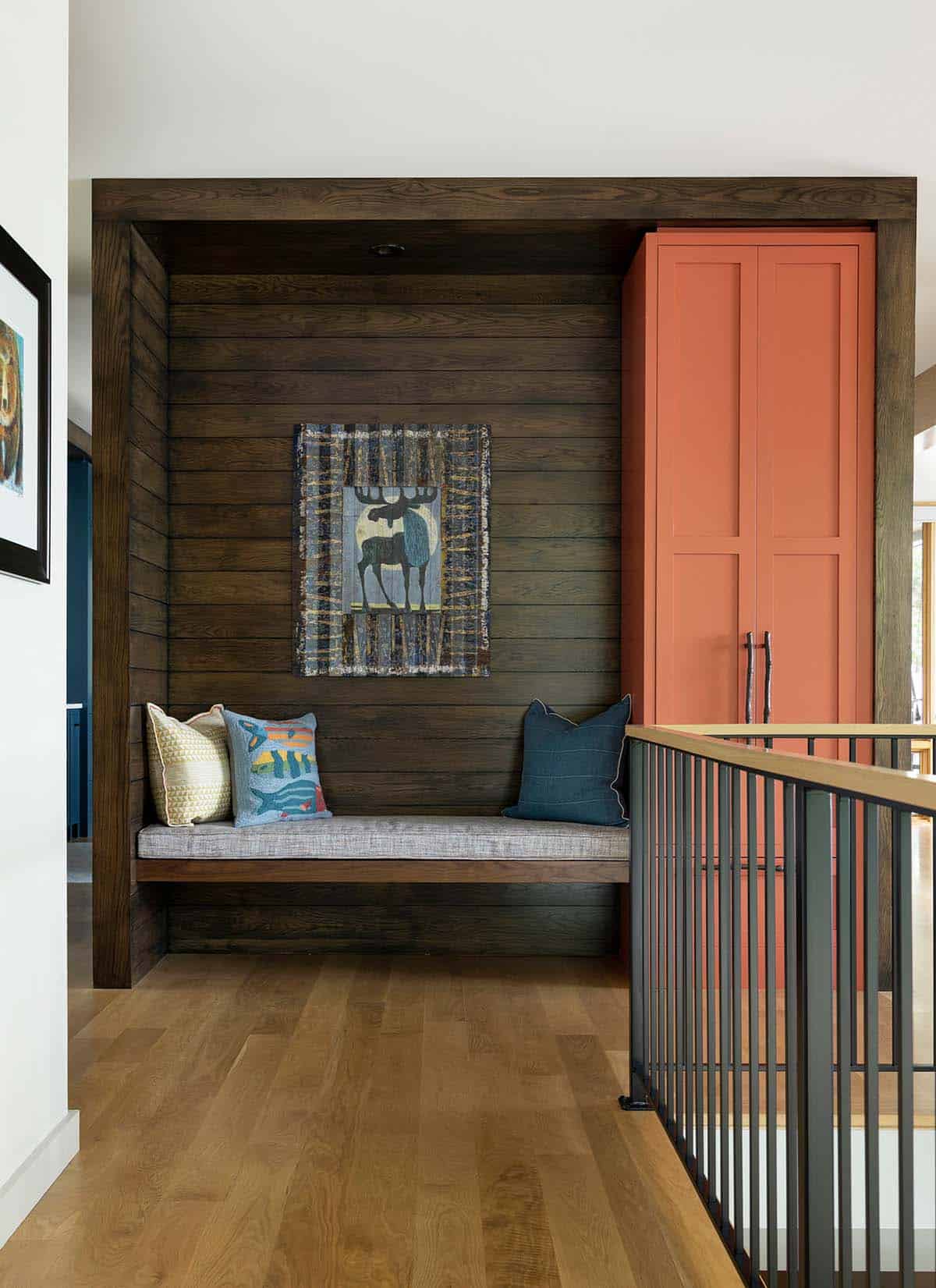 Dark wood bench nook with moose artwork, pillows, and a coral storage cabinet