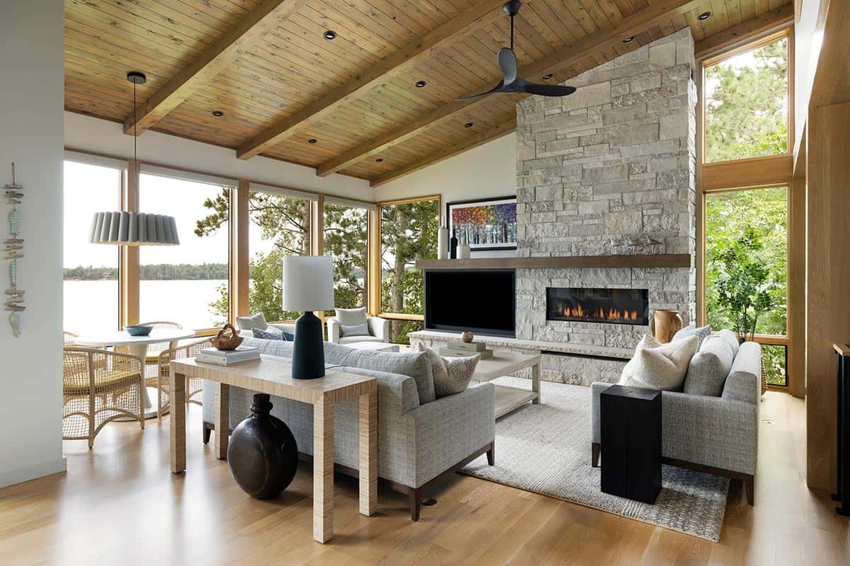 Living room with lake-view windows, stone fireplace, and a pleated pendant over the round table