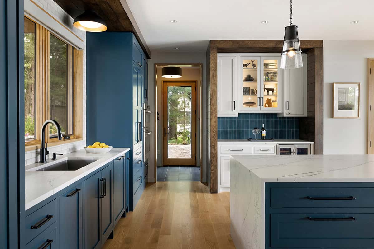 Kitchen with blue cabinetry, glowing glass-front cabinet, and a view down the hall to the back door