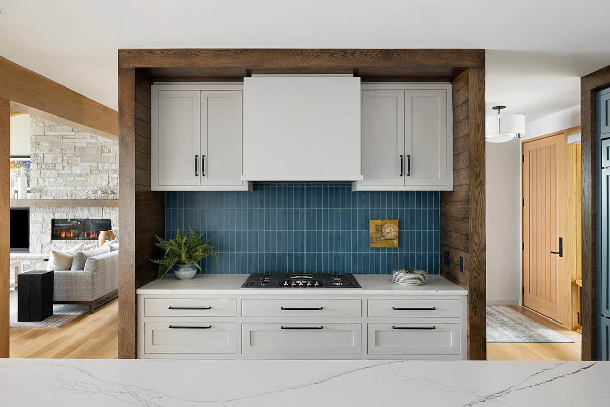 Range alcove with a blue tile backsplash, white hood, and wood-framed surround