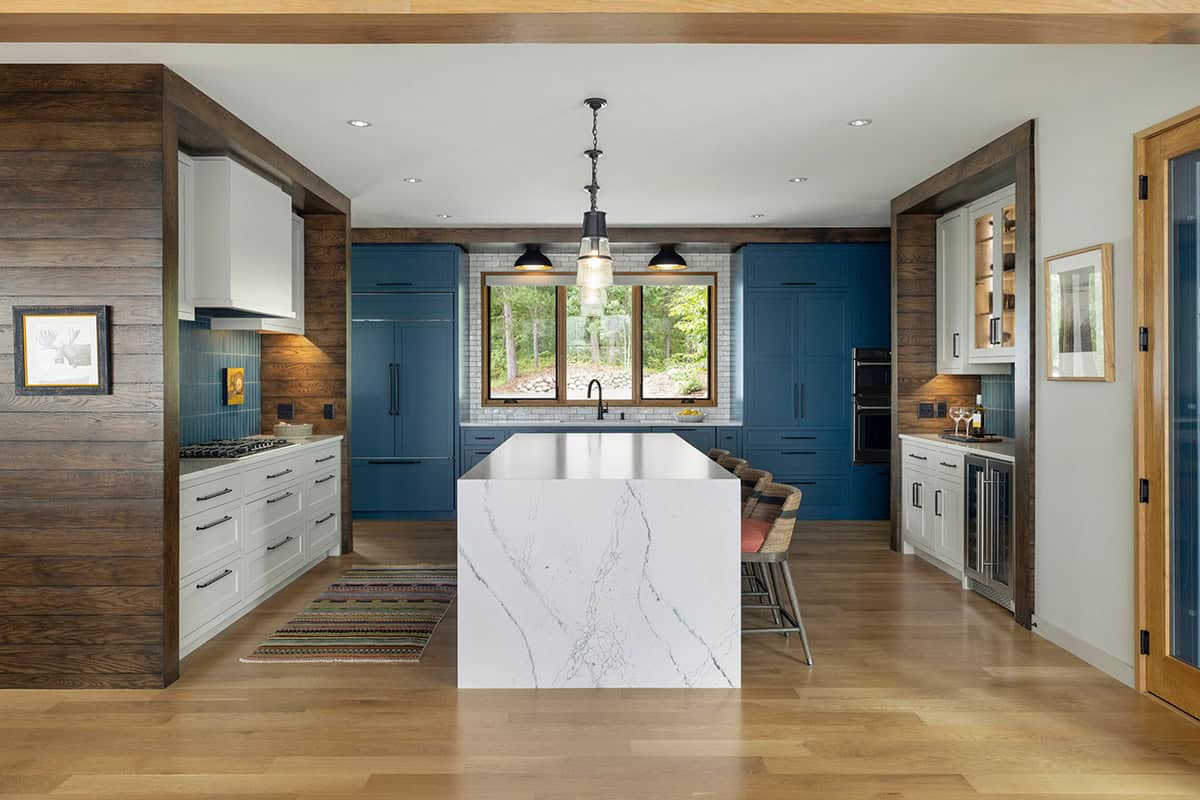 Straight-on view of the kitchen with a marble island, blue cabinets, and a window above the sink