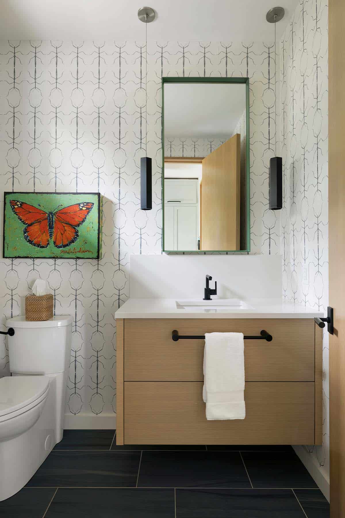 Powder room with bug-patterned wallpaper, floating oak vanity, and a butterfly painting
