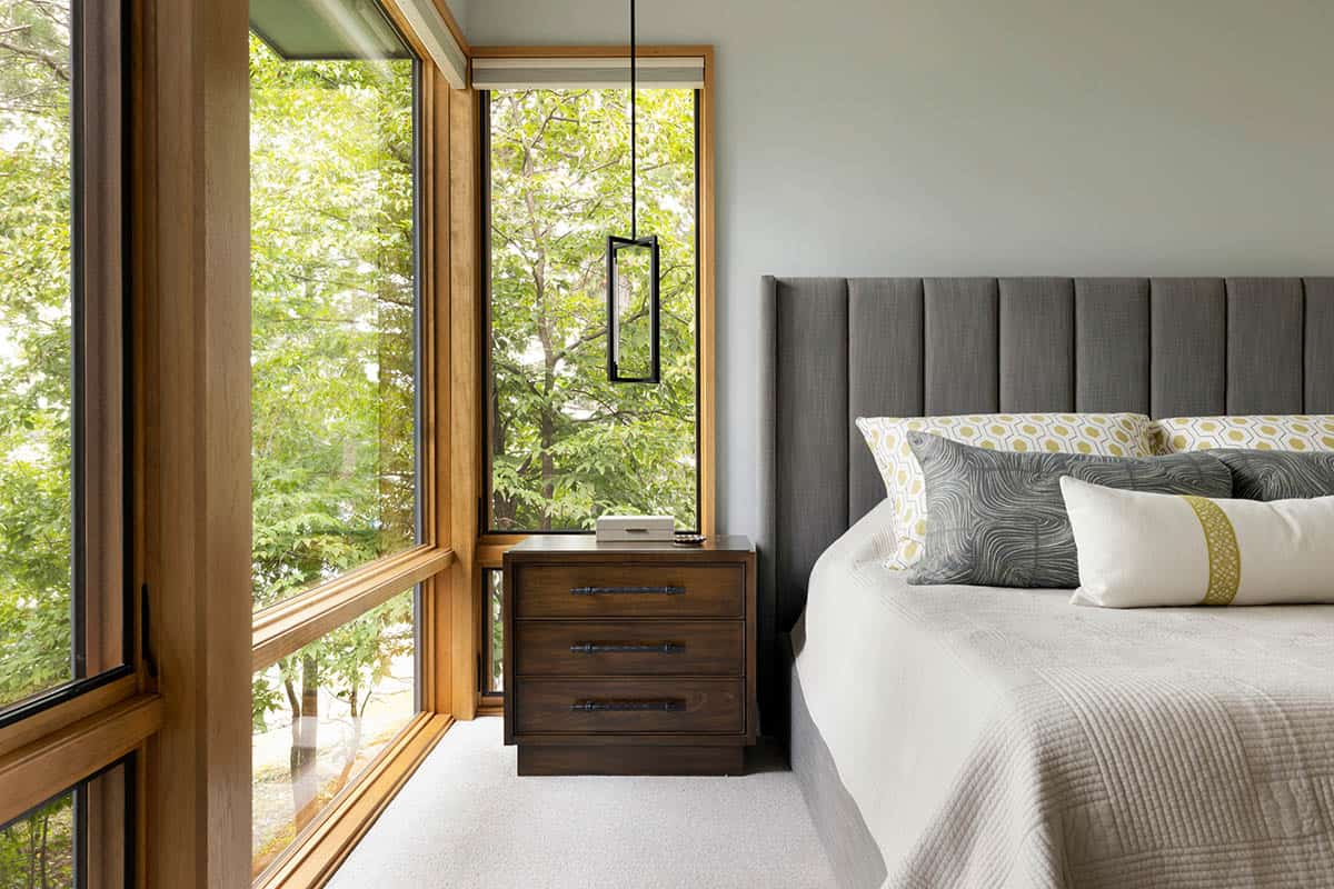 Bedroom with a pendant light, wood-framed corner windows, and a gray upholstered bed