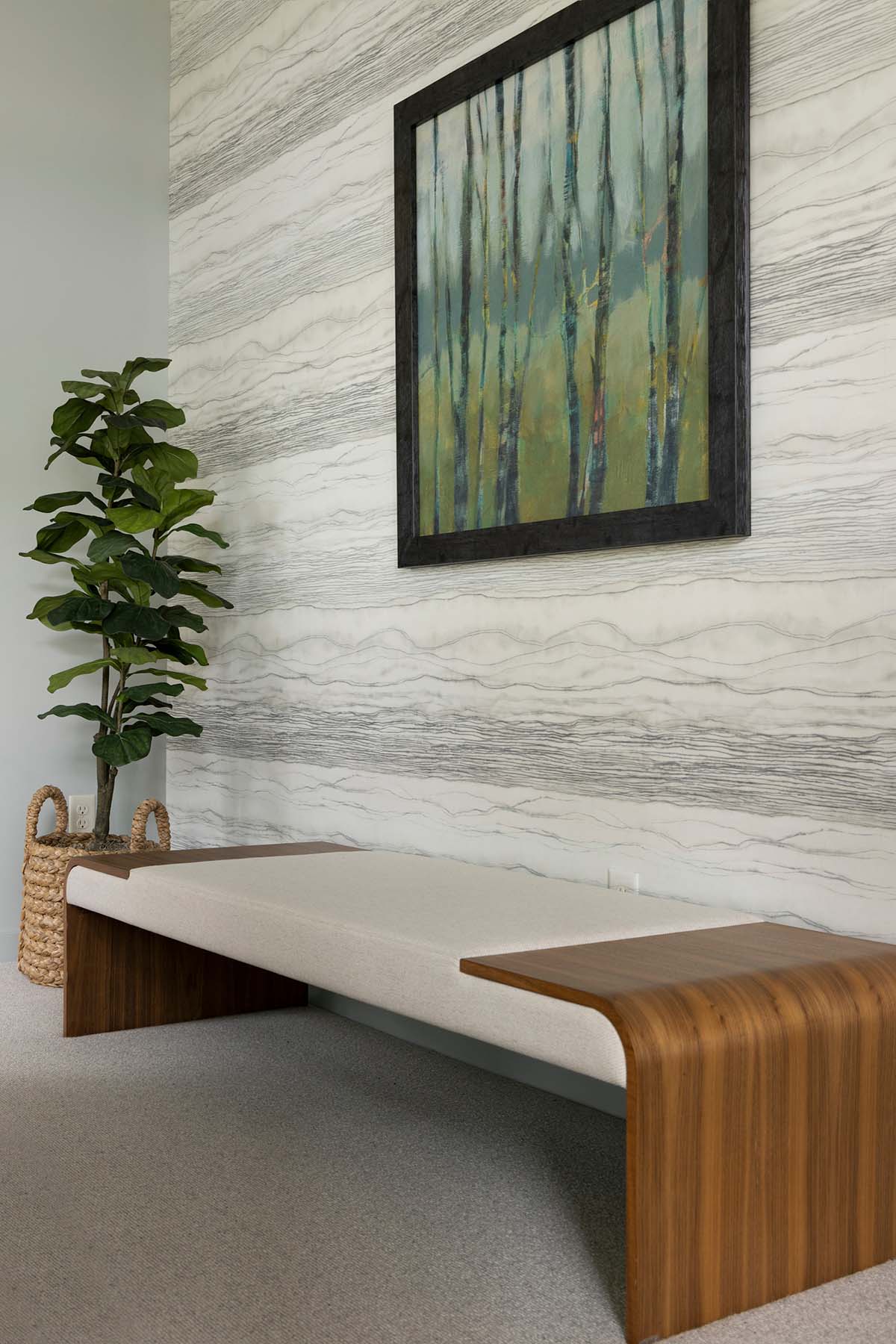 Upholstered bench beneath a framed forest painting on a wallpapered accent wall