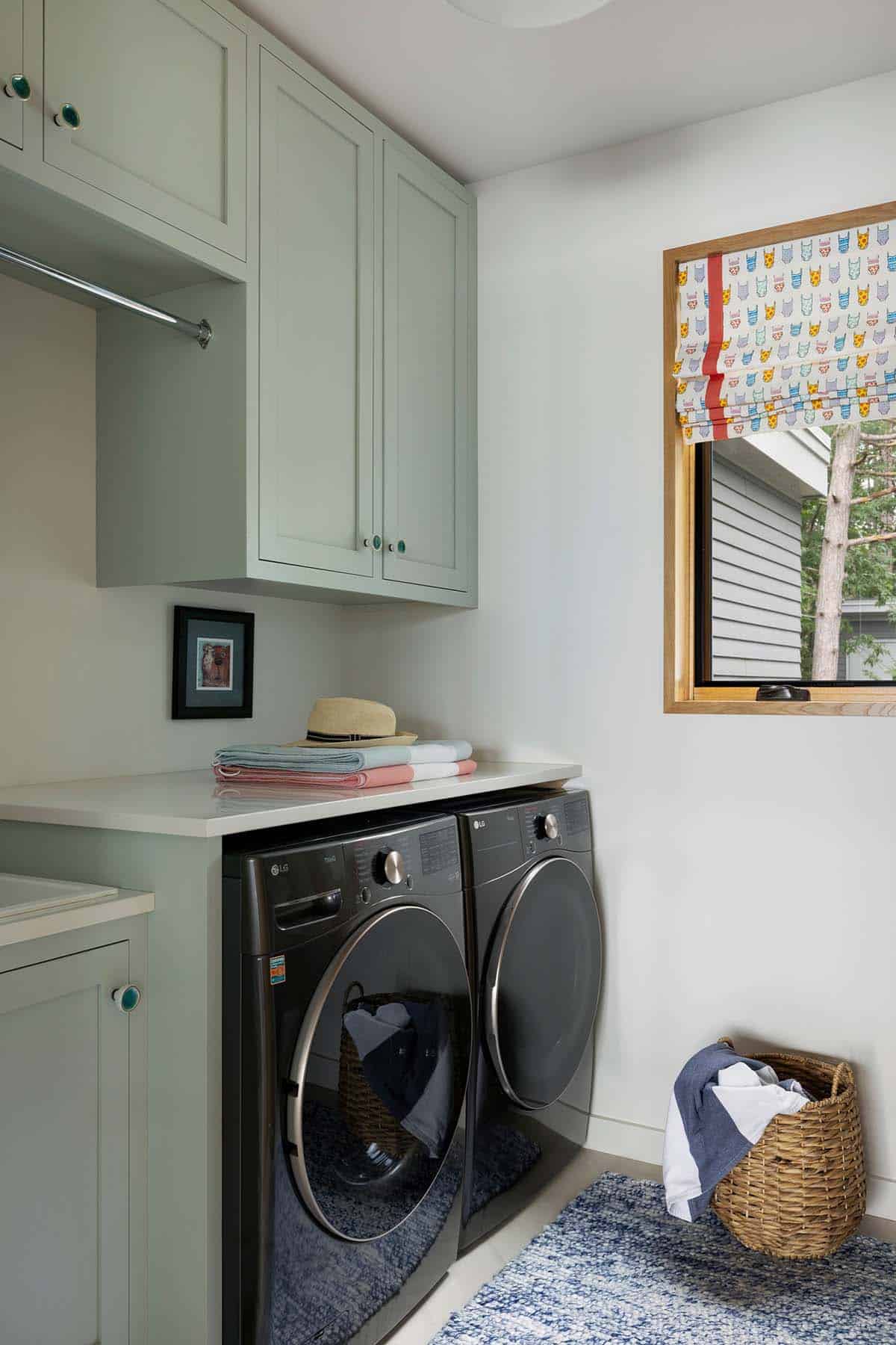 Laundry room with sage cabinets, front-load washer and dryer, and a swimsuit-print shade