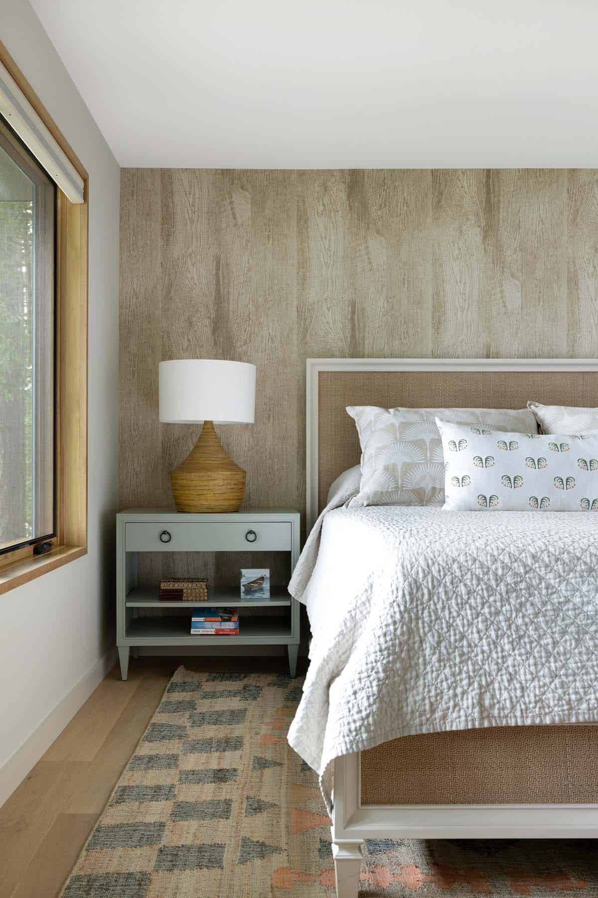Guest bedroom with a woven headboard, wood-look accent wall, and sage bedside table