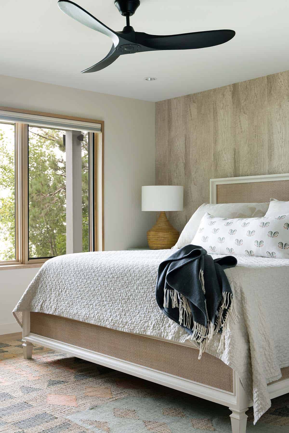 Guest bedroom with a black ceiling fan, navy throw, and a patterned rug