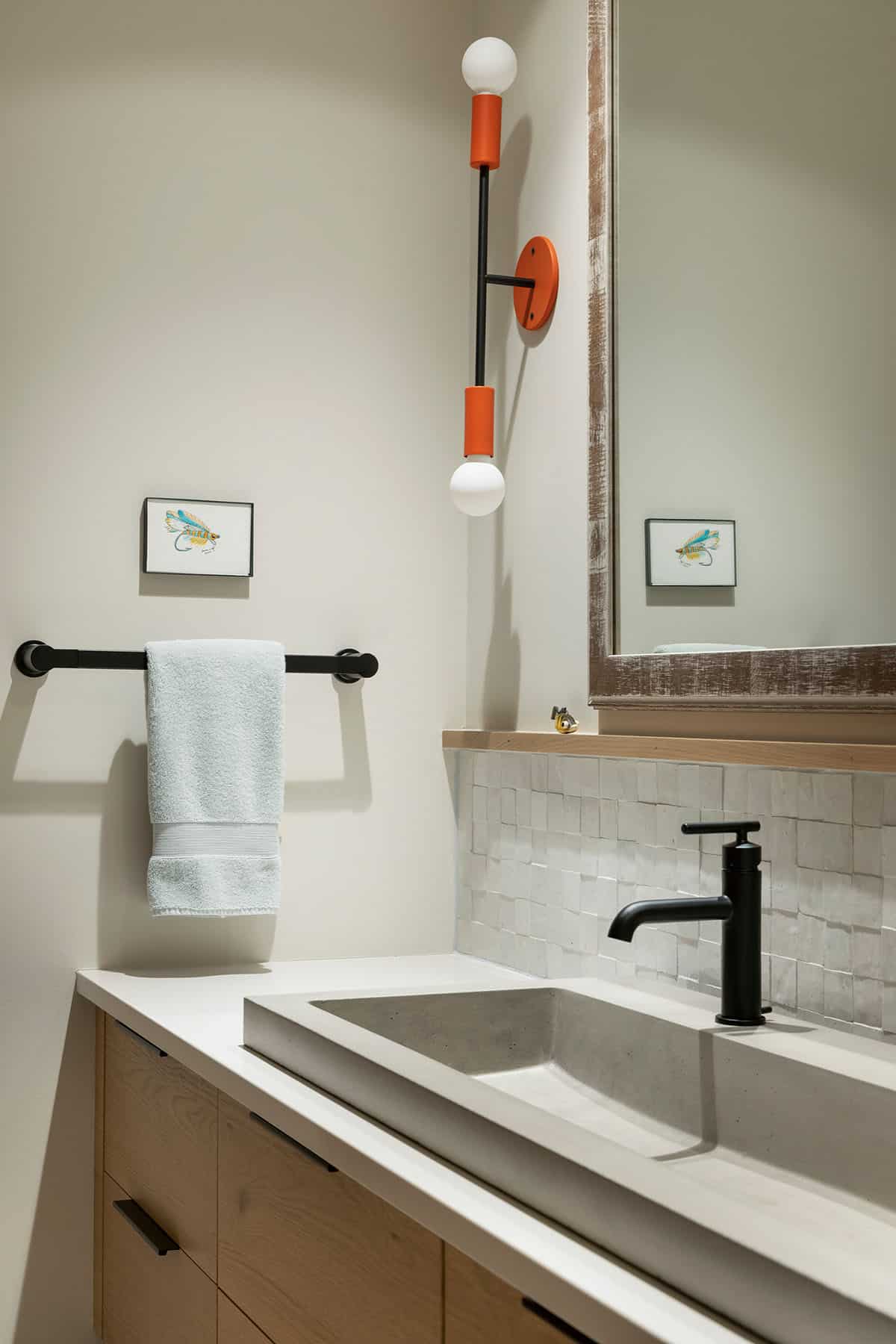 Bathroom detail with an orange sconce, concrete trough sink, and framed fishing fly art