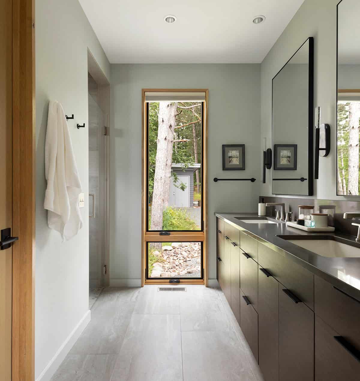 En-suite bathroom with a tall window, dark double vanity, and a glass shower