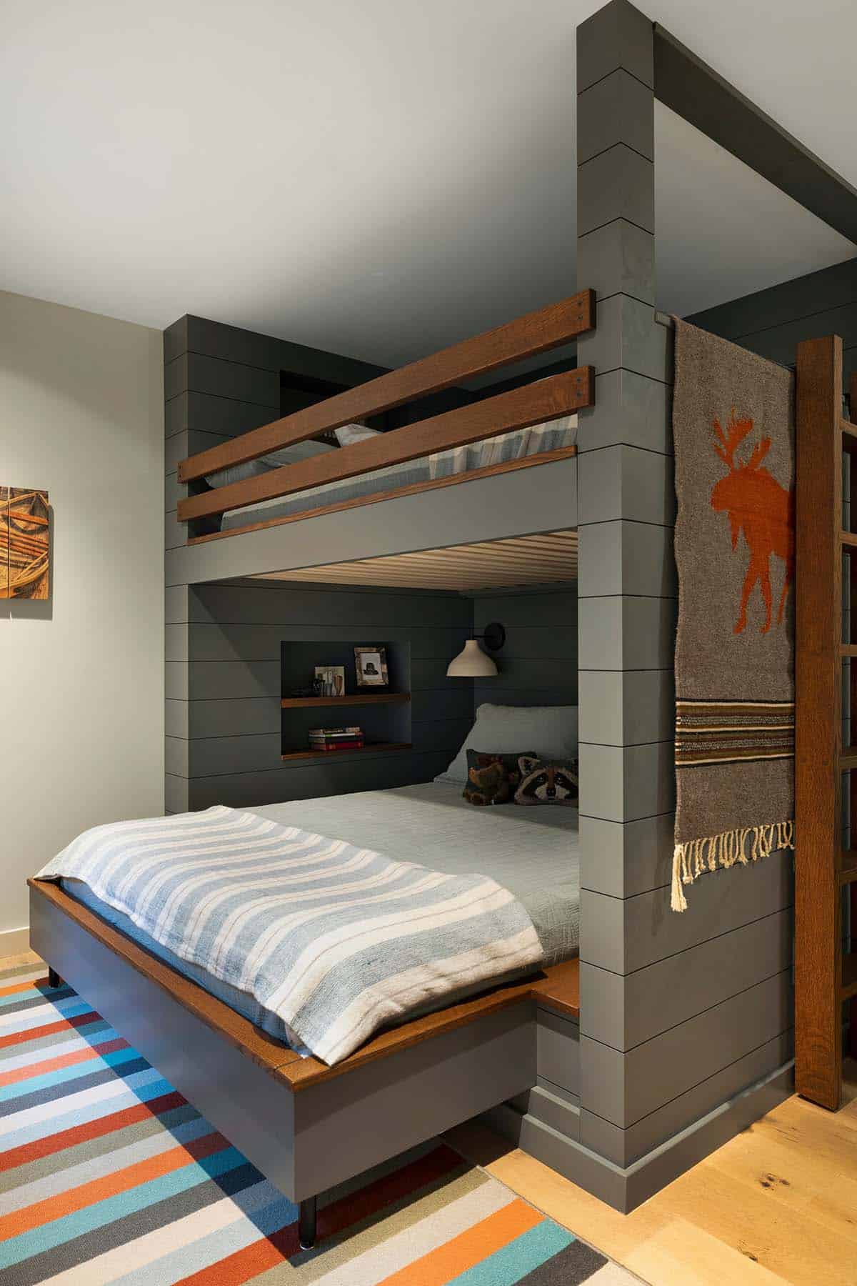 Built-in bunk beds in gray shiplap with oak rails, a moose blanket, and a striped rug