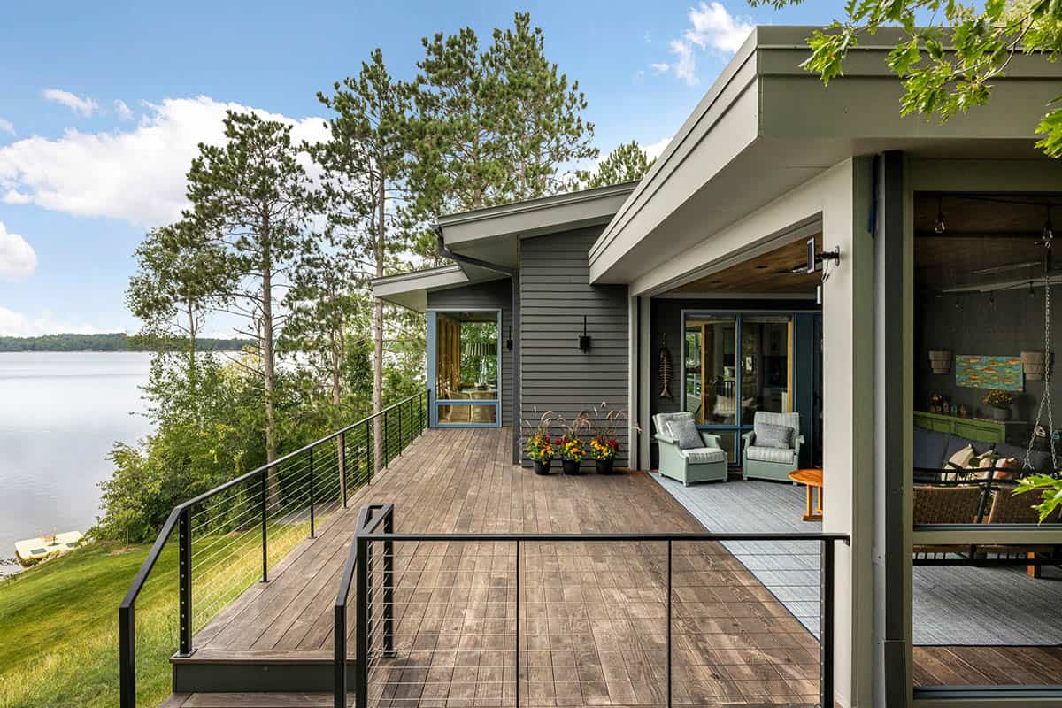 Wood deck with cable railings, pine trees, and a view of the lake from the side of the house