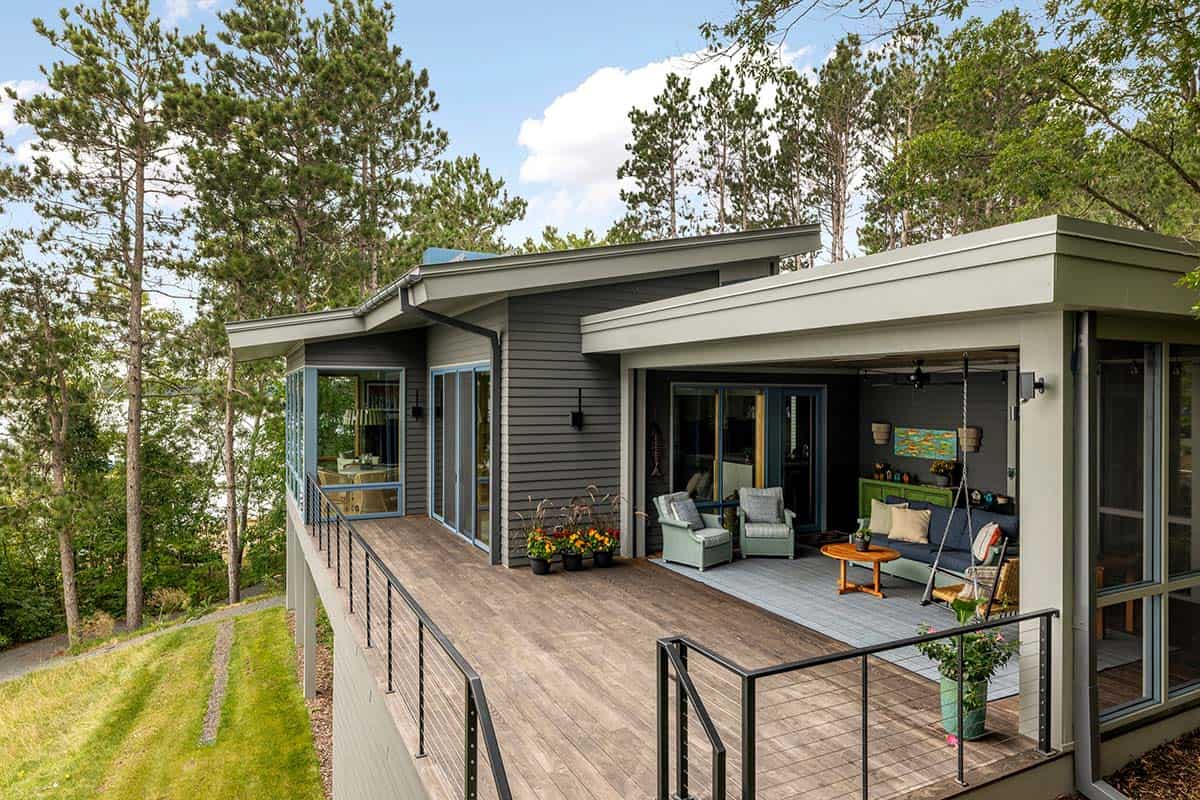 Elevated deck and screened porch seen from the sloped lawn, with pines and sky behind