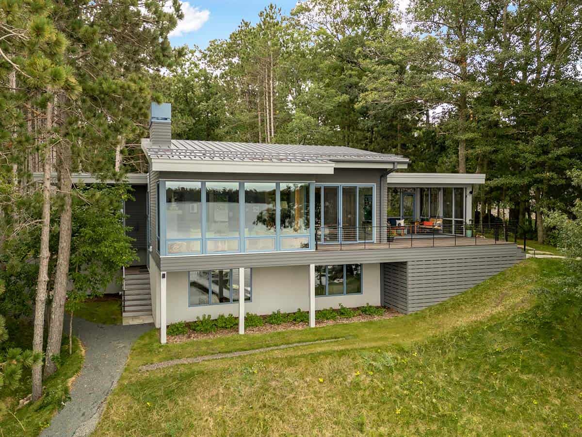 Lake-facing side of the house with a glass sunroom, wood deck, and gravel path through the pines