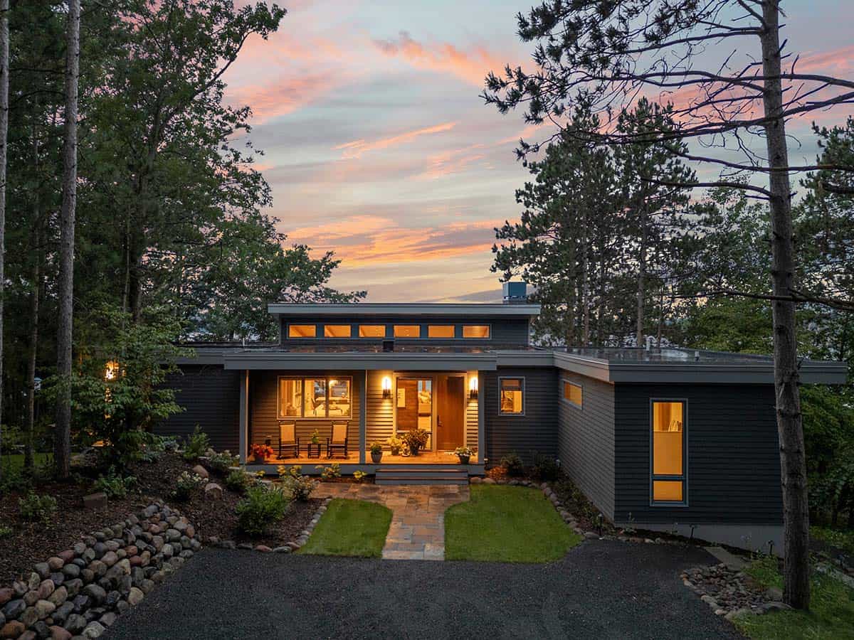 Front of the house at dusk with glowing windows, a lit porch, and a pink sunset sky