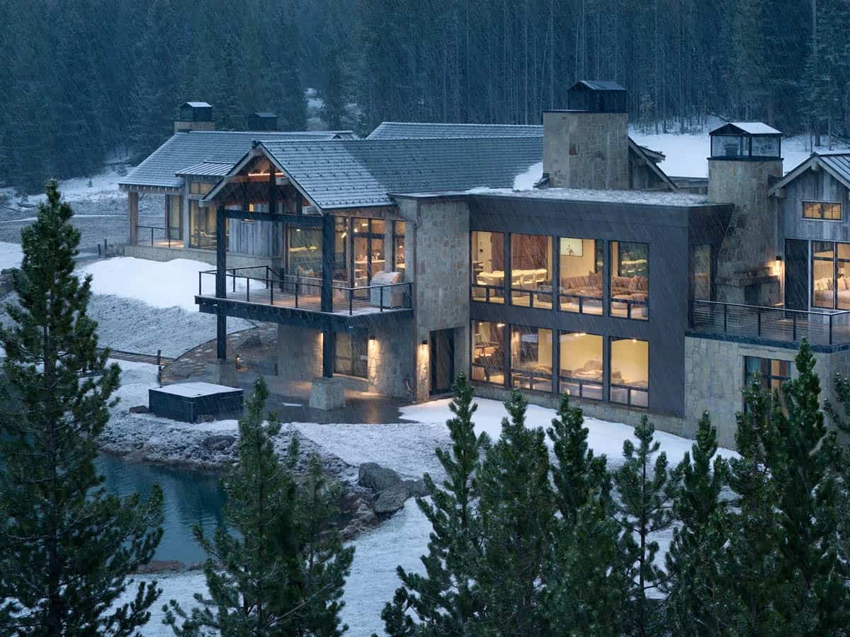 Mountain home with a covered deck and steel-clad wing in falling snow