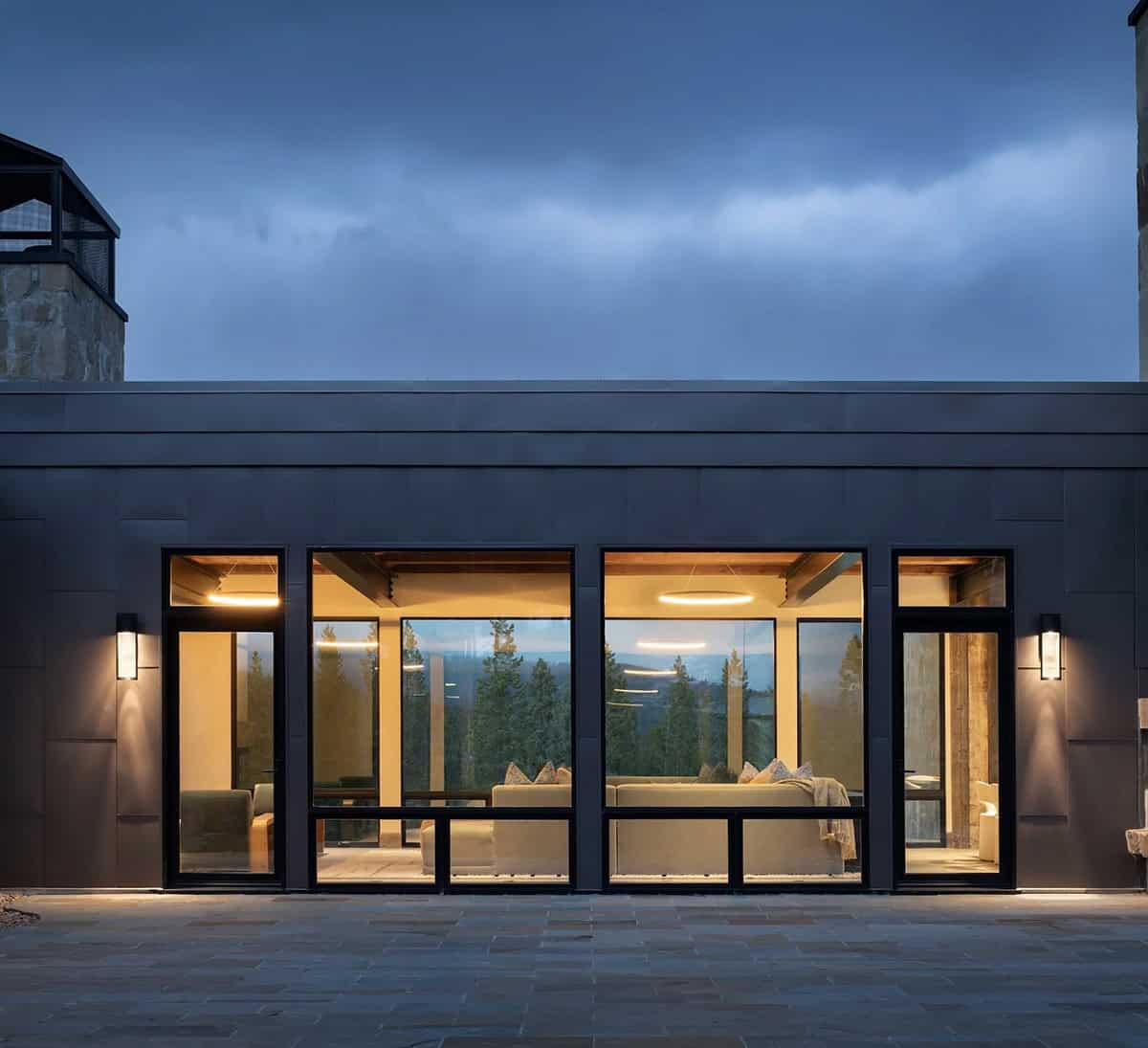 Steel-clad living room wing with tall windows on a flagstone terrace at dusk