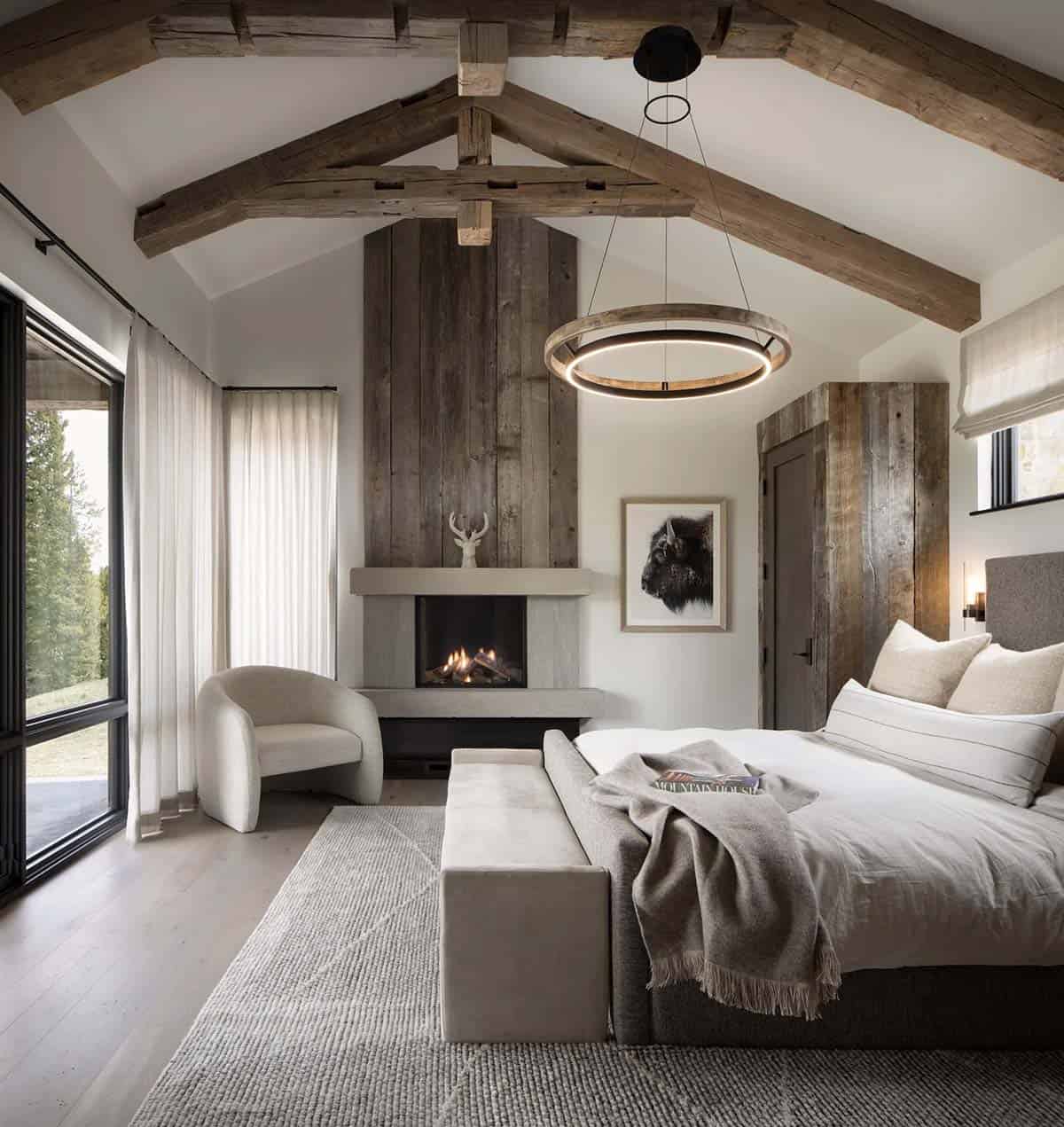 Vaulted bedroom with timber trusses, ring chandelier, and a corner fireplace