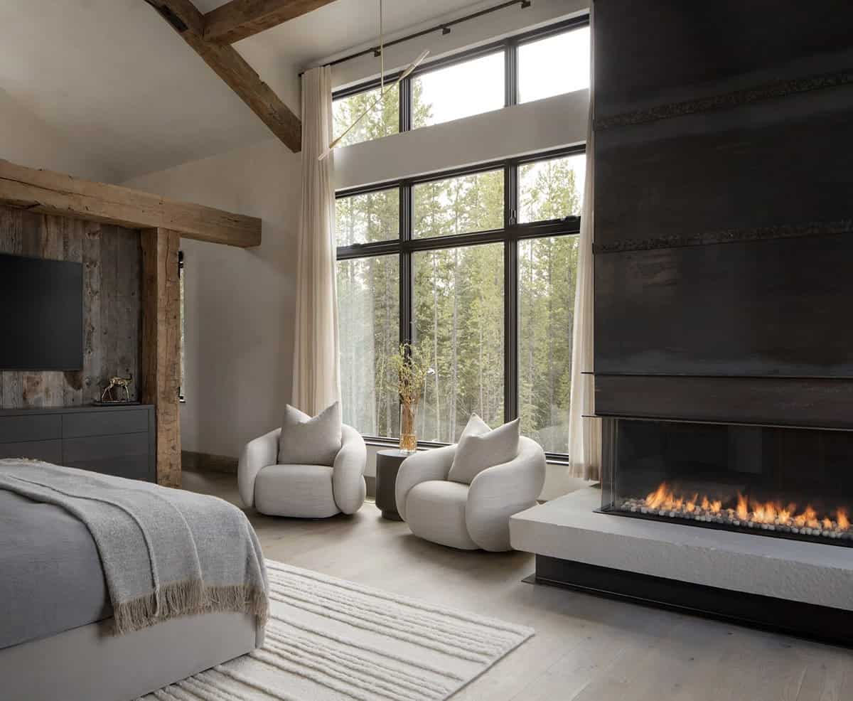 Primary bedroom with a steel-clad fireplace and two swivel chairs by tall windows