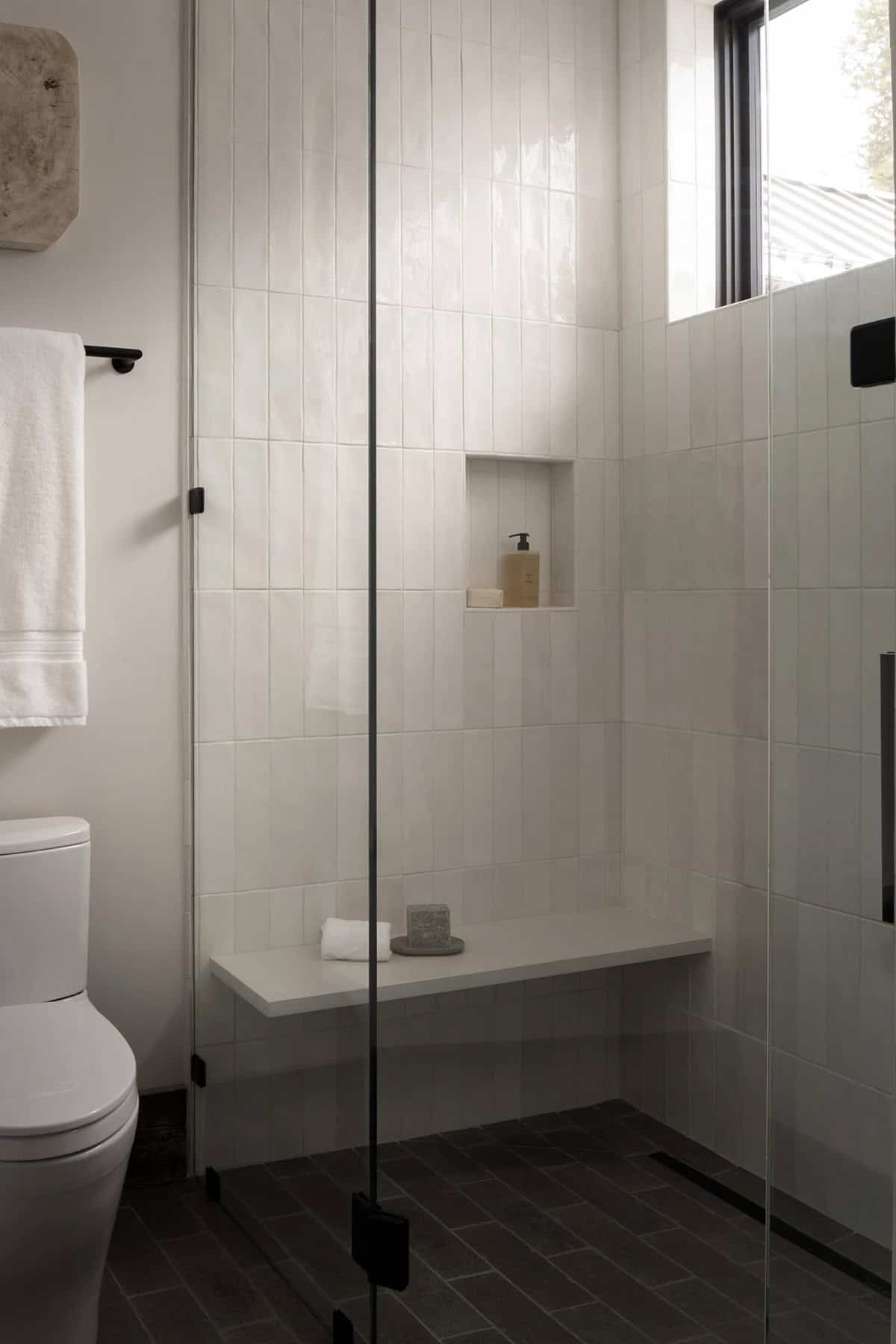 Walk-in shower with white vertical tile, a floating bench, and dark stone floor