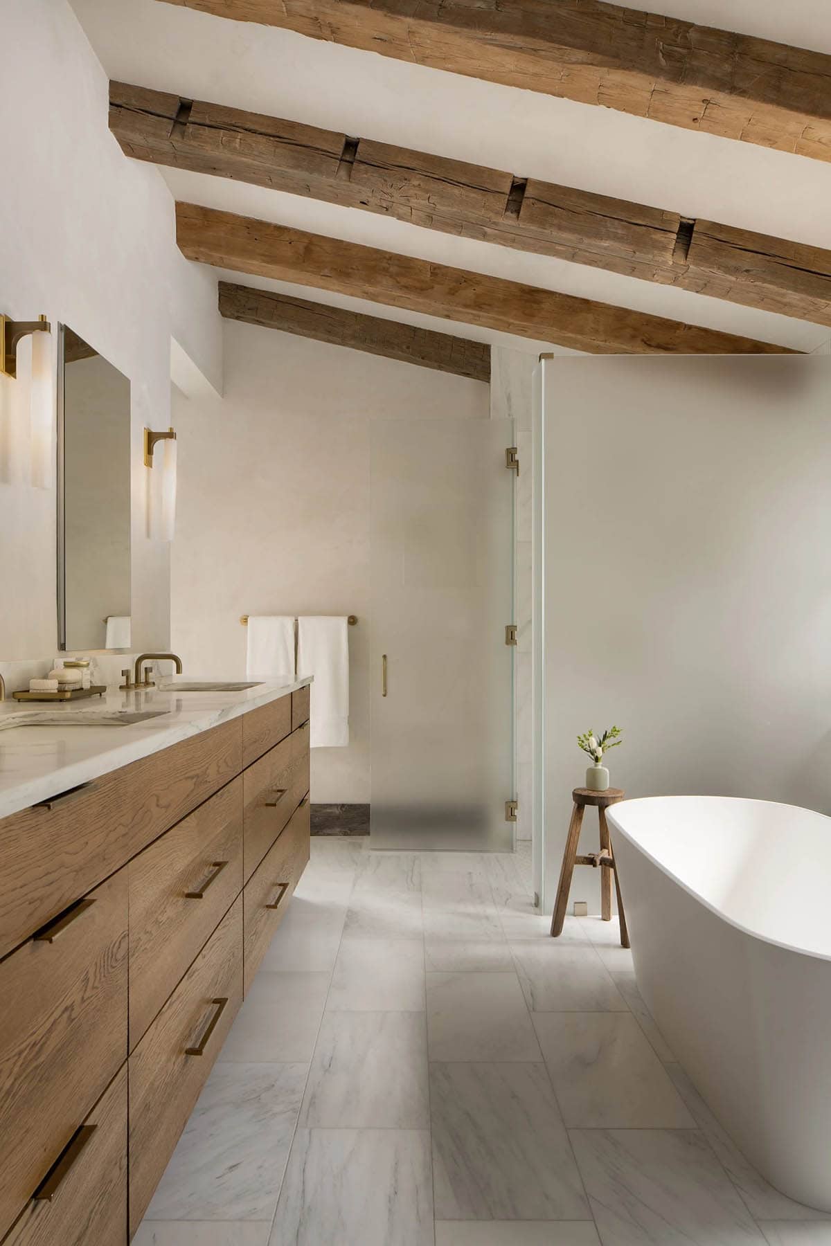 Primary bathroom with a freestanding tub, wood vanity, and timber beams