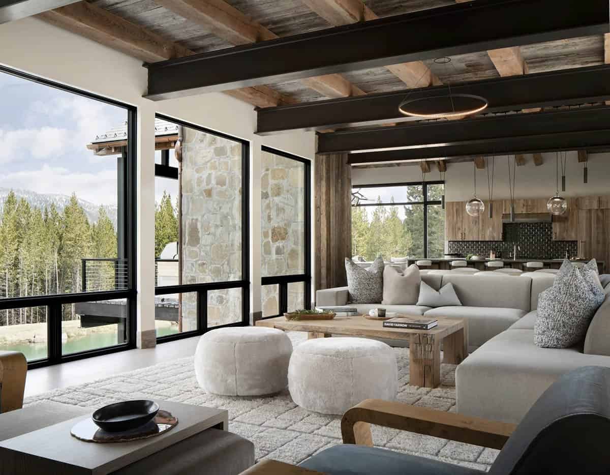 Living room with steel beams, a sectional, and shearling poufs facing a pond