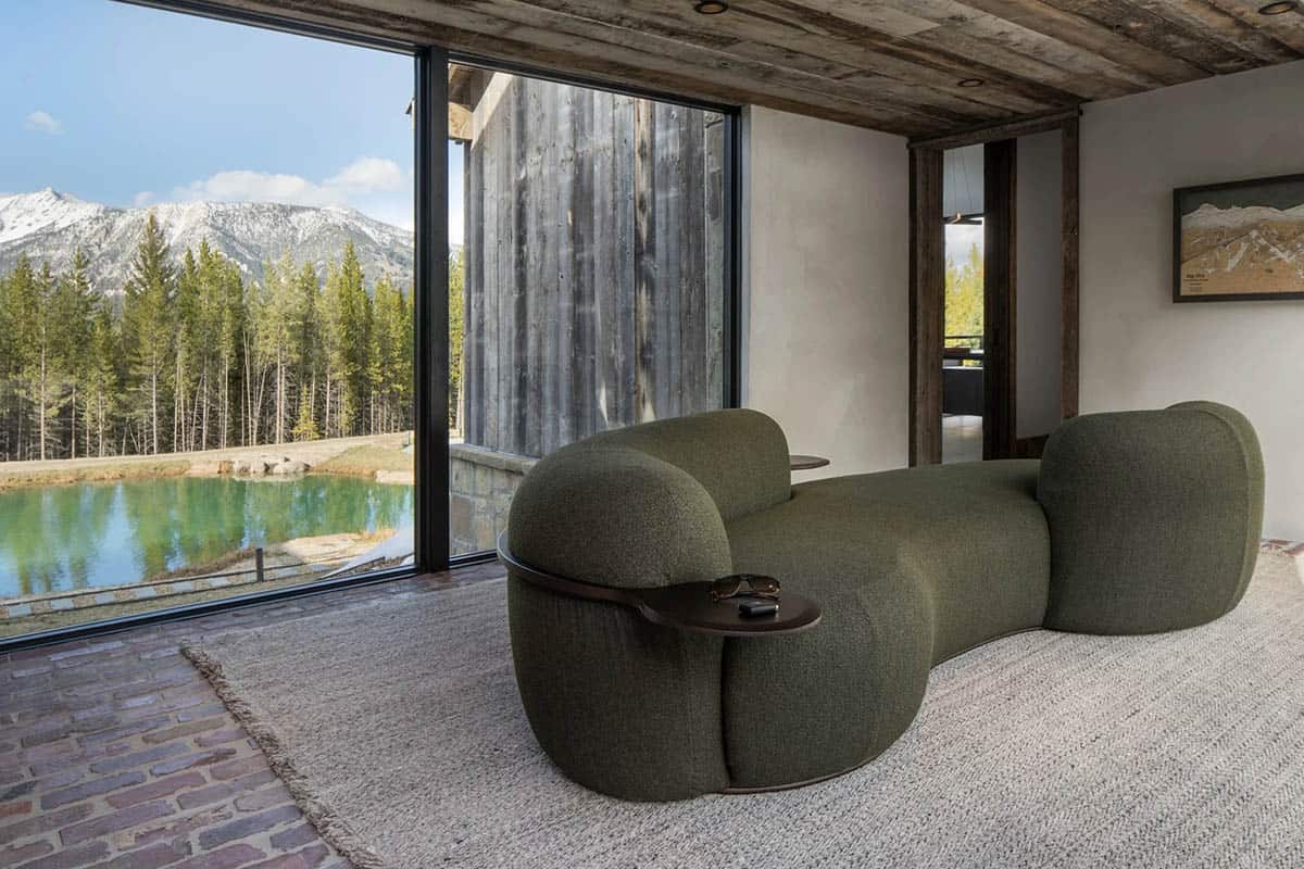 Curved green sofa in a glass breezeway overlooking a pond and mountains