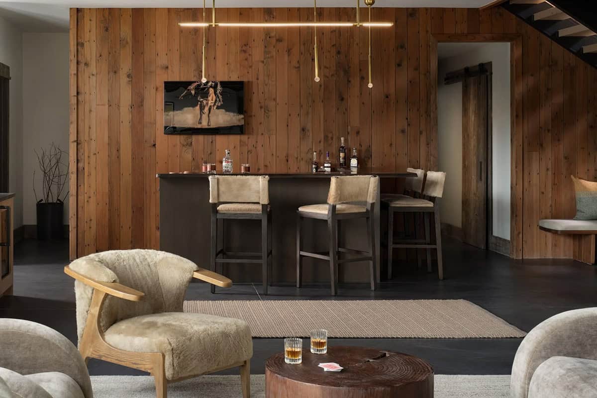 Lower-level bar with wood plank walls, shearling stools, and a brass chandelier