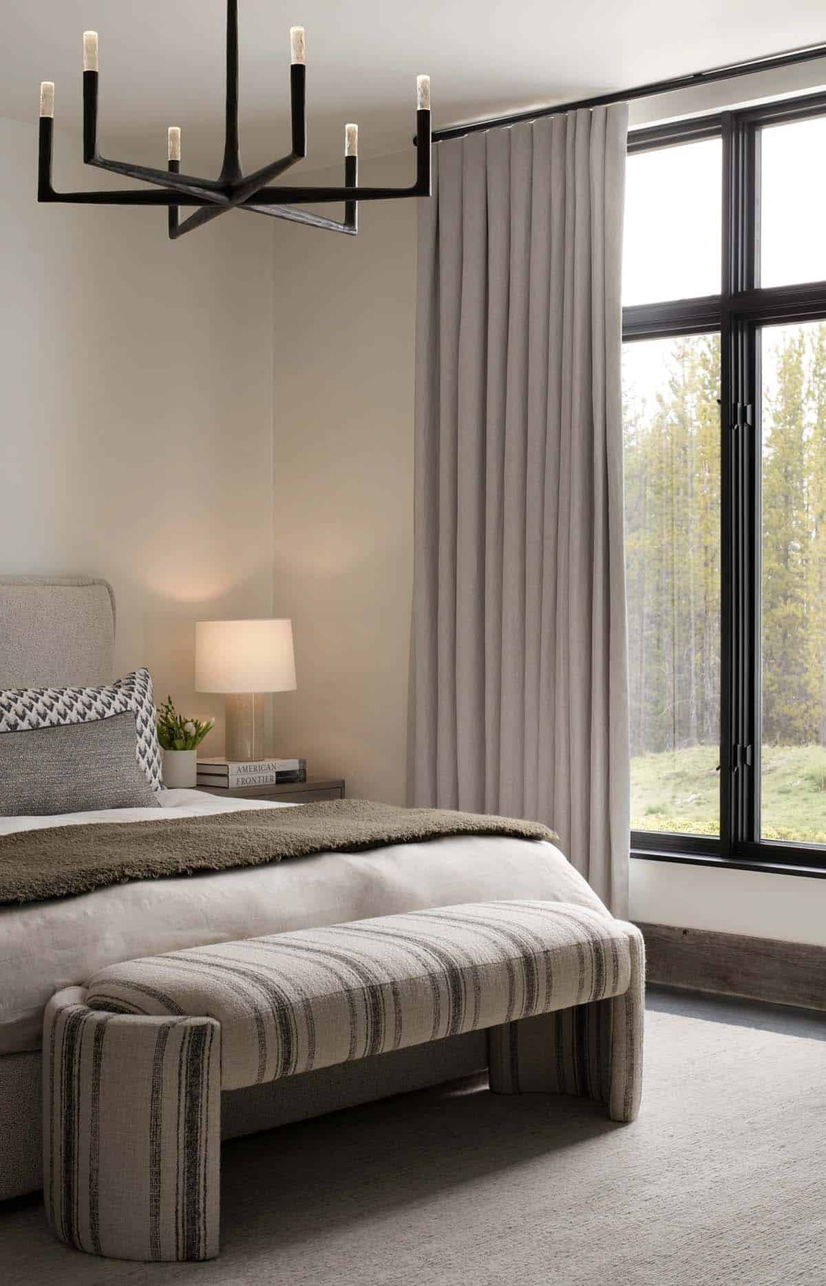 Guest bedroom with a black chandelier, striped bench, and forest view