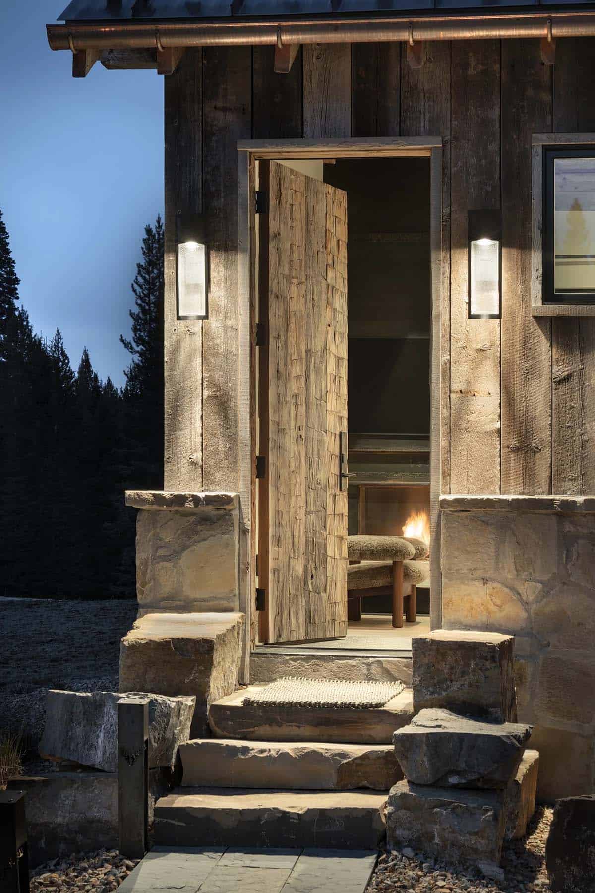 Hand-hewn wood door open to a fireplace, with stone steps at dusk