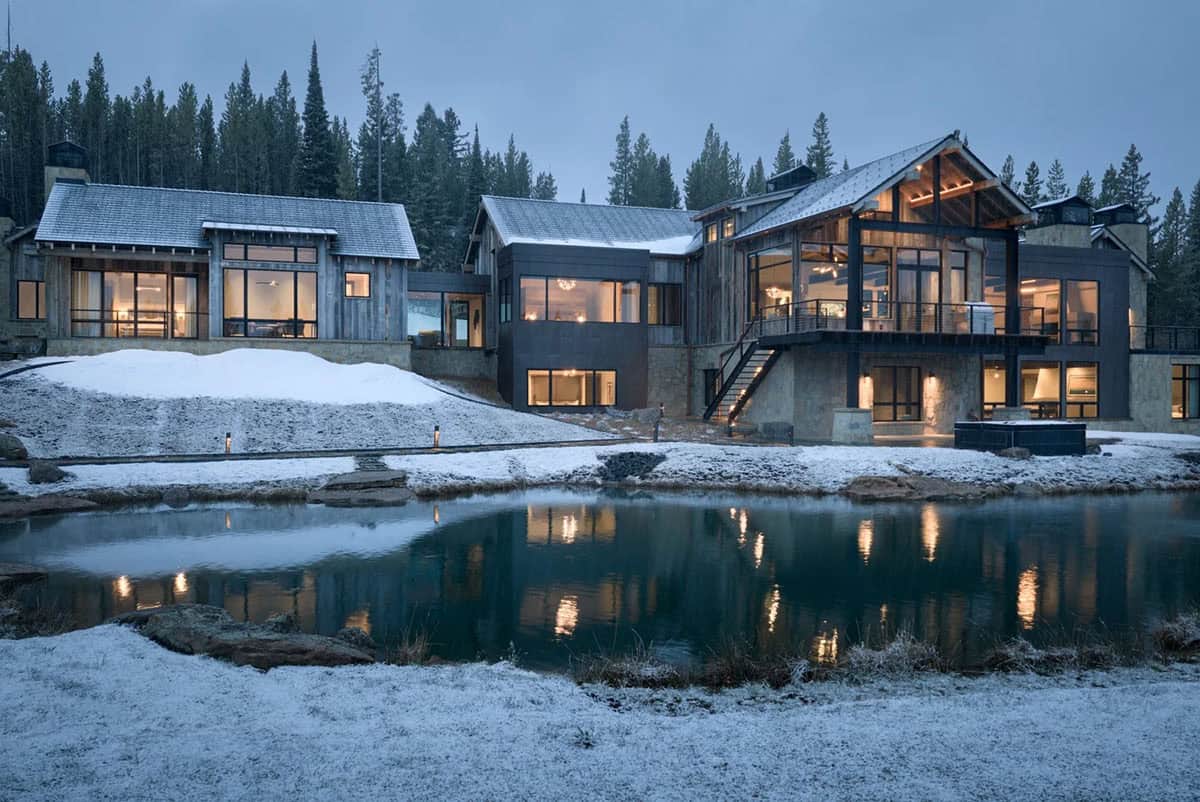 Mountain home with a covered deck and stairs beside a pond at dusk