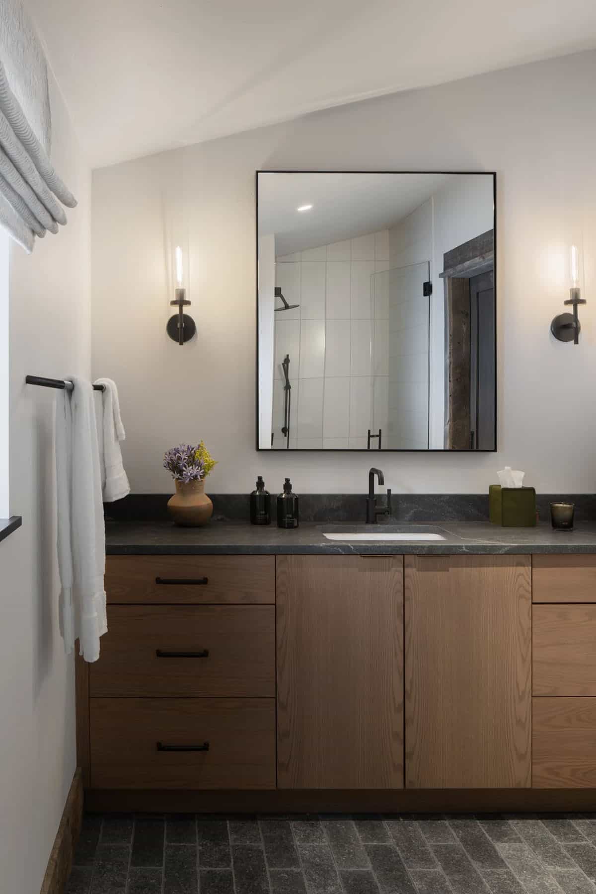 Bathroom with an oak vanity, dark stone countertop, and black mirror