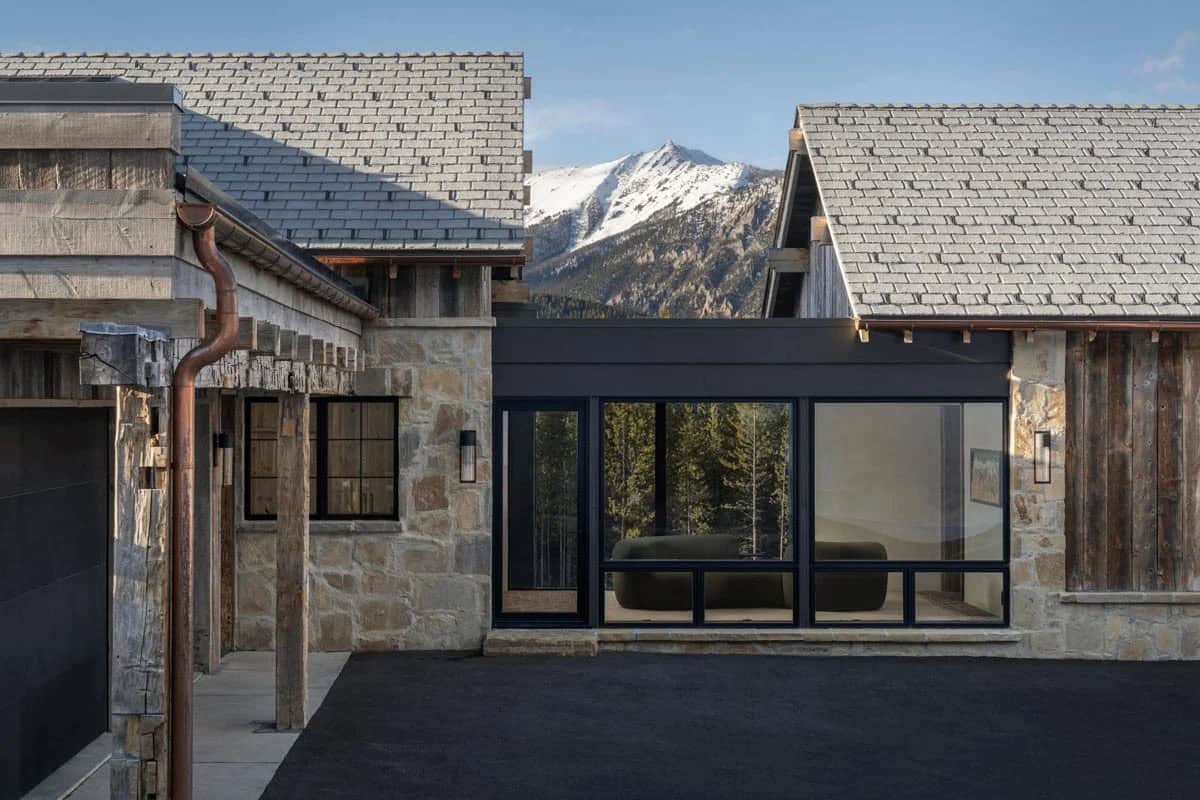 Glass breezeway between stone and wood buildings with a mountain peak behind