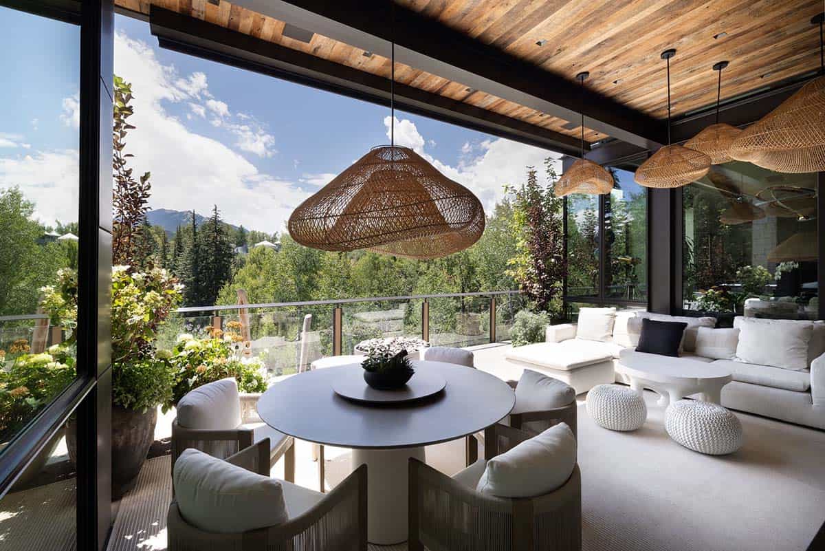 Outdoor dining and lounge area with a round table, rattan pendants, and mountain views