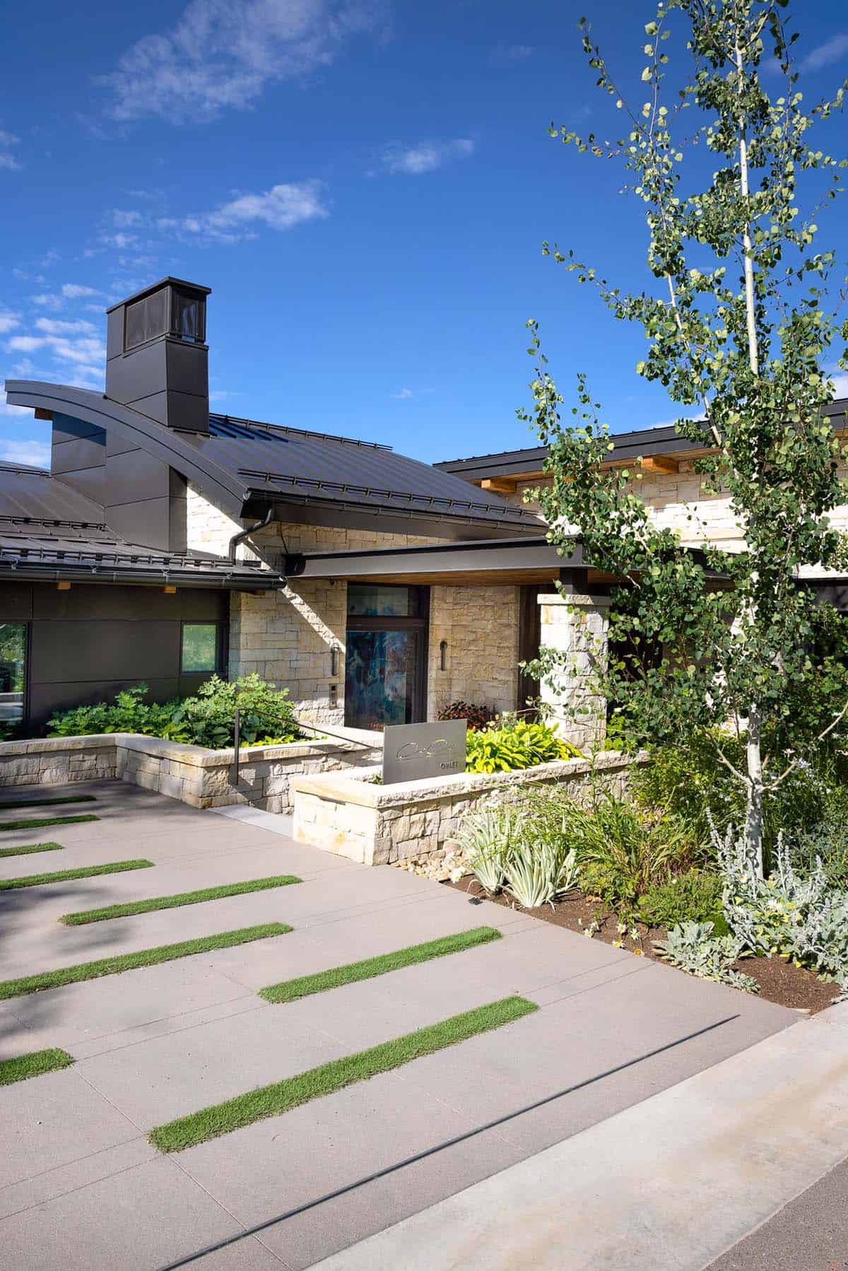 Home entry with stone walls, curved metal roof, and a concrete drive with grass strips