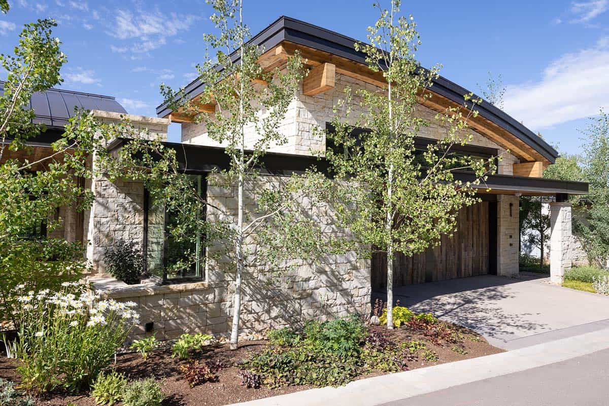 Garage with a curved timber roofline, stone walls, and a reclaimed wood door, framed by aspens