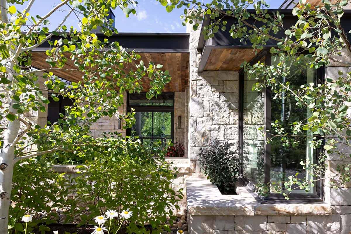 Stone facade with large corner window and wood-clad overhang, seen through aspen leaves