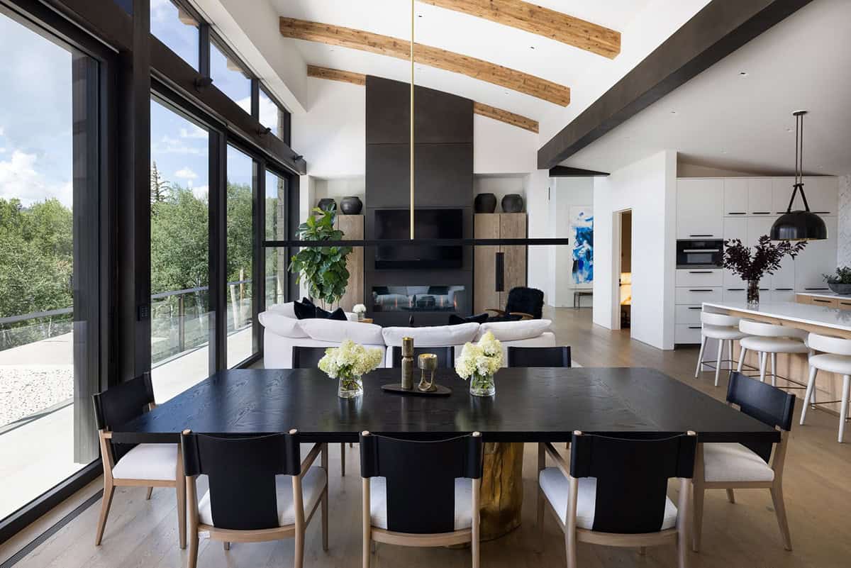 Open dining area with a black table, vaulted beamed ceiling, and kitchen beyond