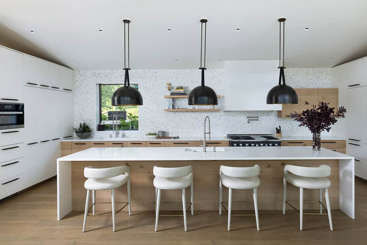 White kitchen with an oak-front island, black dome pendants, and a herringbone tile backsplash