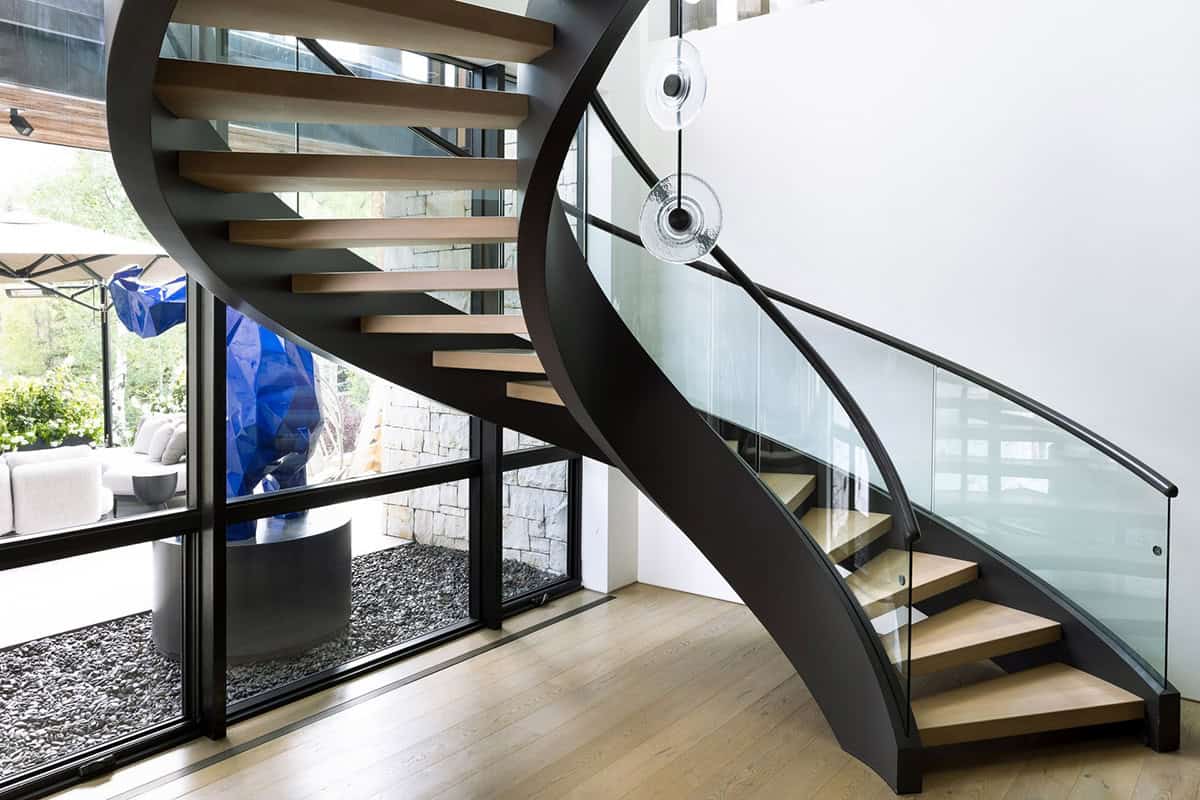 Curved black staircase with oak treads beside windows showing a blue sculpture outside