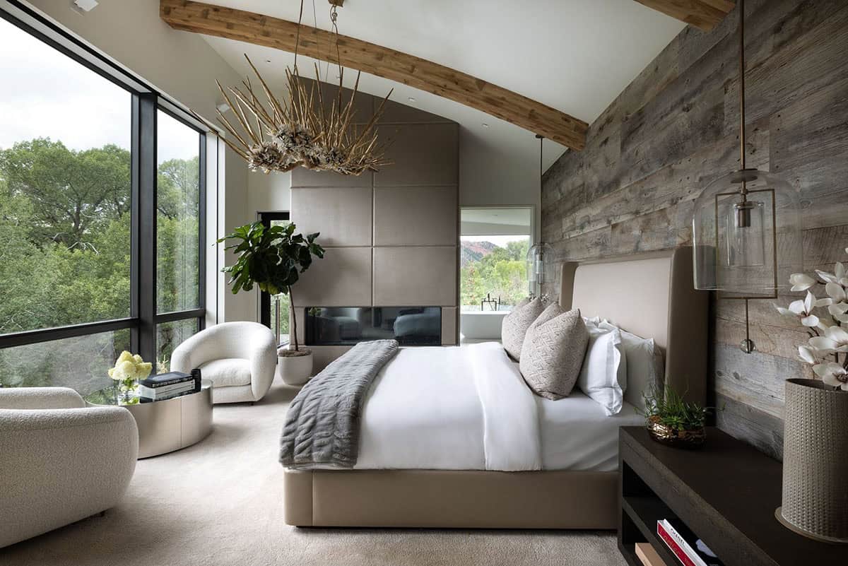 Primary bedroom with a reclaimed wood accent wall, curved ceiling beam, and driftwood-style chandelier