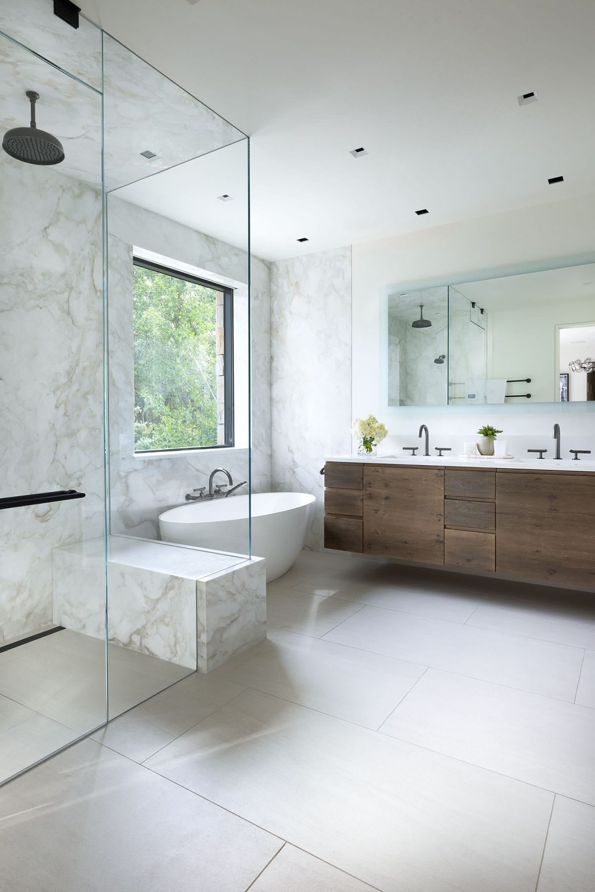 Spa-style bathroom with marble walls, glass shower, freestanding tub, and a floating wood vanity