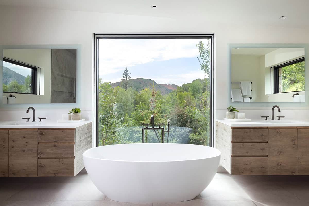 Freestanding tub centered before a large picture window, flanked by two wood vanities