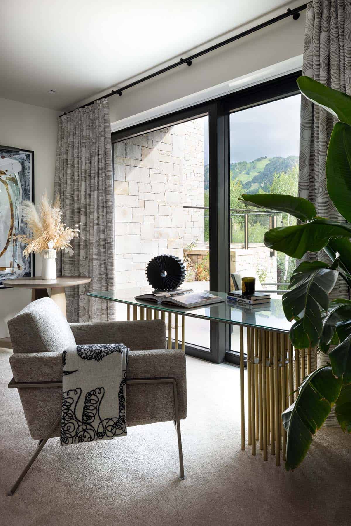 Sitting nook with a boucle armchair, brass-based glass desk, and a sliding door to the terrace
