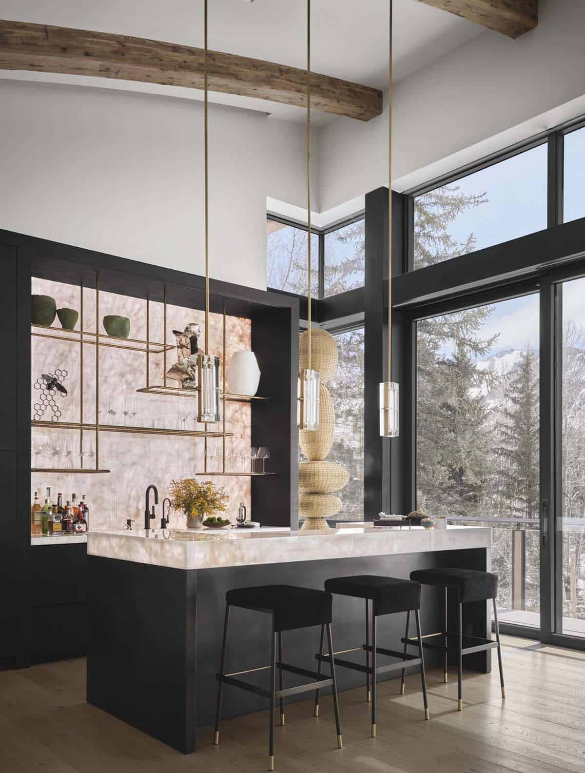 Double-height bar with glass pendants, a lit onyx island, and tall windows onto snowy evergreens