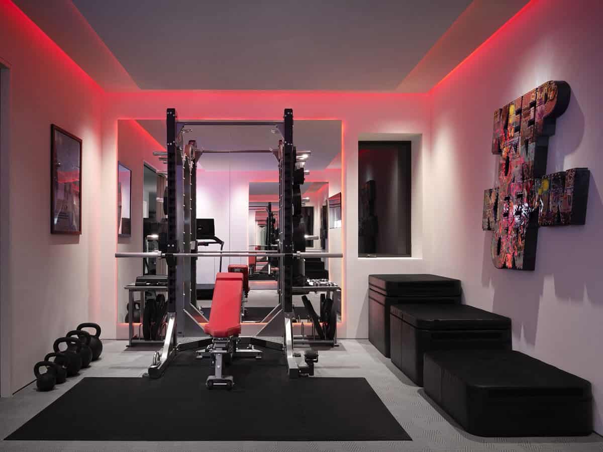 Home gym with red LED cove lighting, squat rack, mirrored wall, kettlebells, and plyo boxes