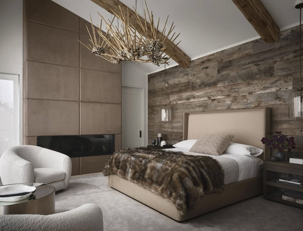 Primary bedroom with a reclaimed wood wall, upholstered fireplace surround, twig chandelier, and faux fur throw