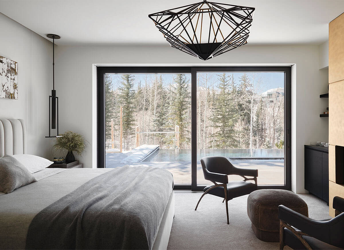 Bedroom with a sliding glass door overlooking a snowy infinity pool, geometric black chandelier, and leather armchair
