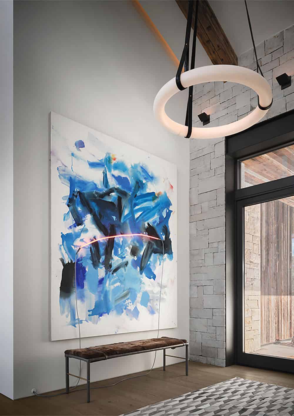 Entry with a large blue abstract painting, ring-shaped pendant, and stacked stone wall