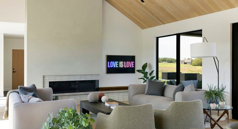 Living room with a linear fireplace in white tile, a neon Love Is Love sign, gray sofas, boucle chairs and a tall window to the prairie