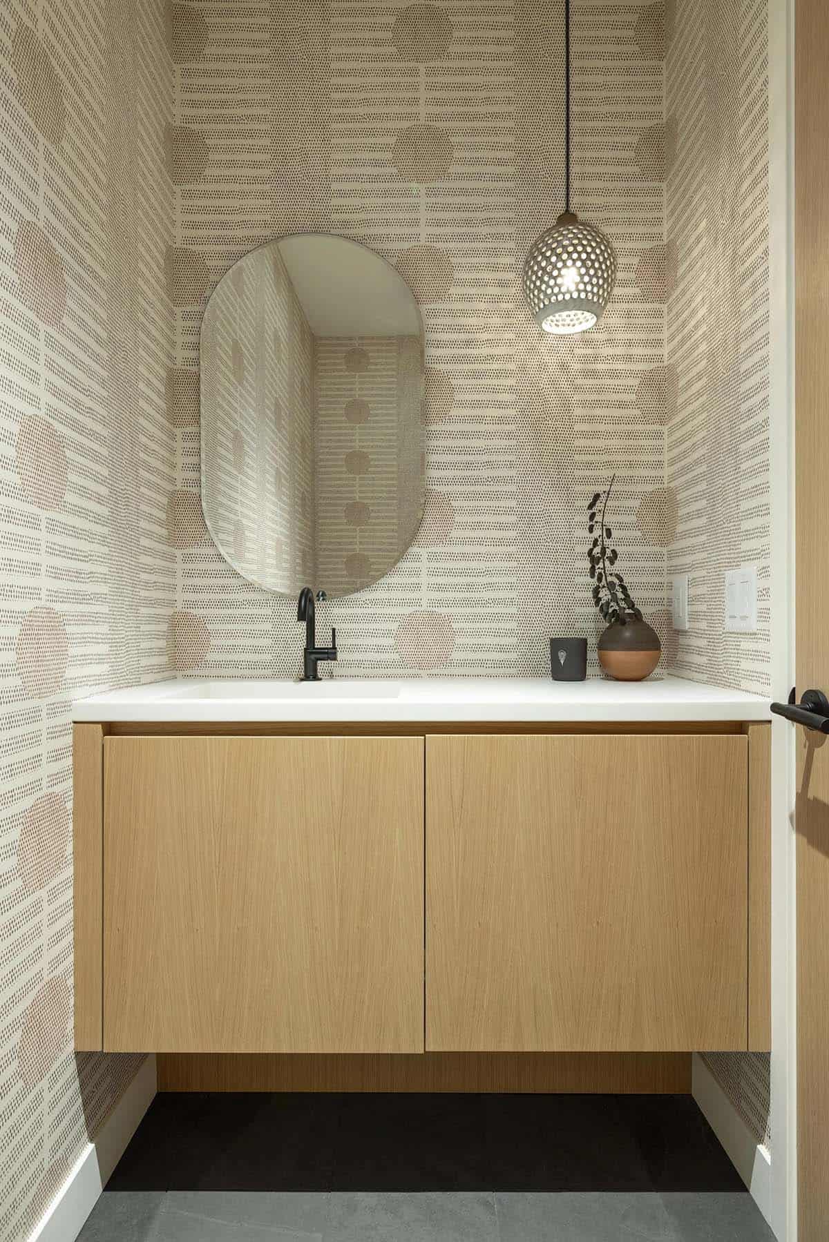 Powder room with dotted pattern wallpaper, an oval mirror, a pierced ceramic pendant and a floating white oak vanity with a black faucet